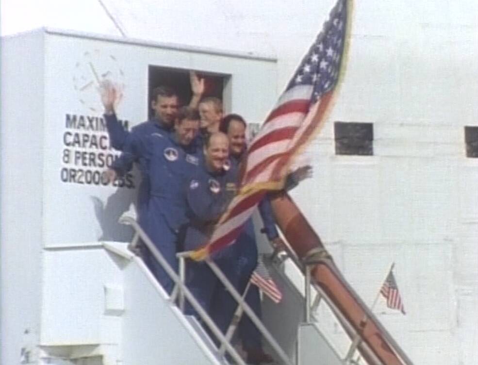 The astronauts exit Discovery waving a large American flag