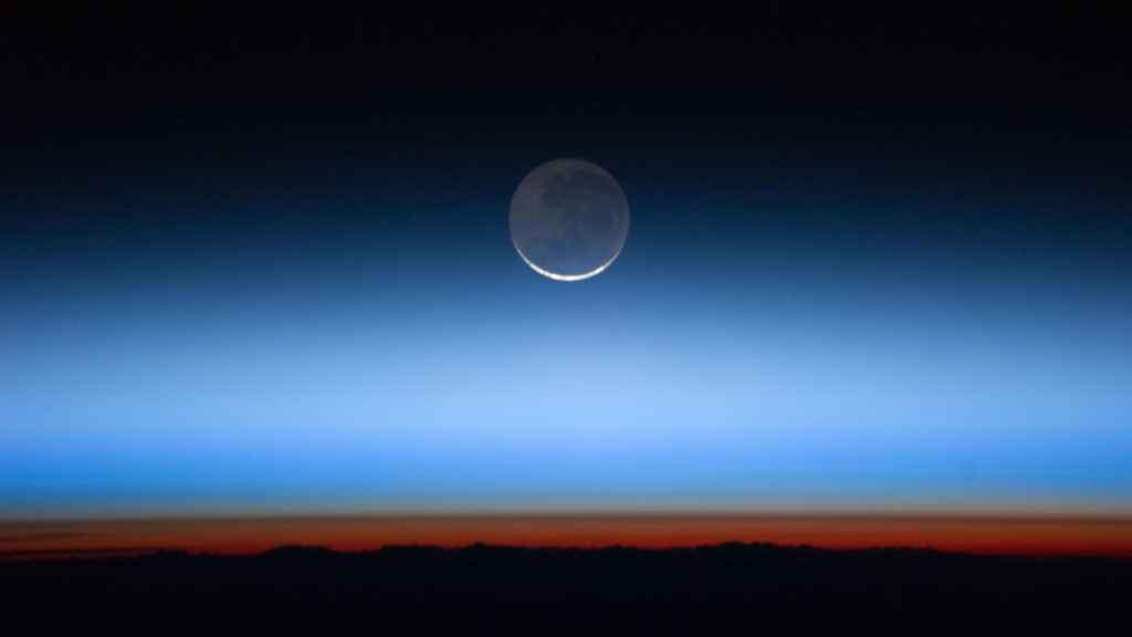 A crescent moon is just above the horizon at sunrise.