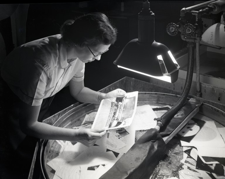 Woman examines prints in darkroom.