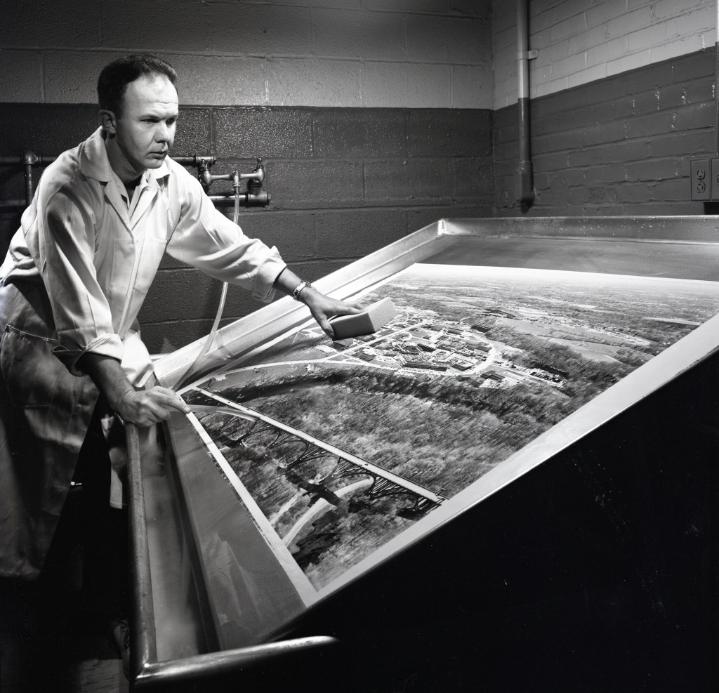 Man in darkroom working on oversized photograph.