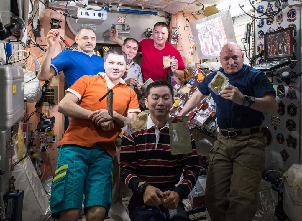 Expedition 45 crew members Mikhail B. Korniyenko, left, Oleg D. Kononenko, and Sergei A. Volkov of Roscosmos, NASA astronaut Kjell N. Lindgren, Kimiya Yui of the Japan Aerospace Exploration Agency, and NASA astronaut Scott J. Kelly pose before the Thanksgiving dinner table