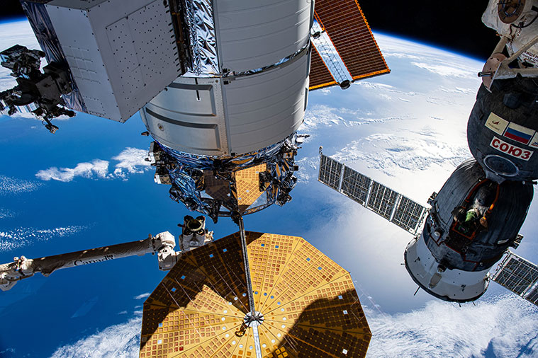 The Cygnus space freighter and the Soyuz MS-24 crew ship (at right) are pictured attached to the station. At lower left, the Canadarm2 robotic arm prepares to grapple Cygnus.