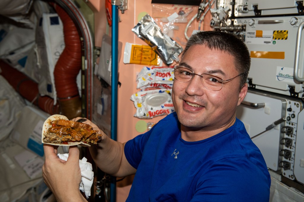 NASA astronaut and Expedition 67 Flight Engineer Kjell Lindgren prepares to enjoy a taco during dinner time aboard the International Space Station.