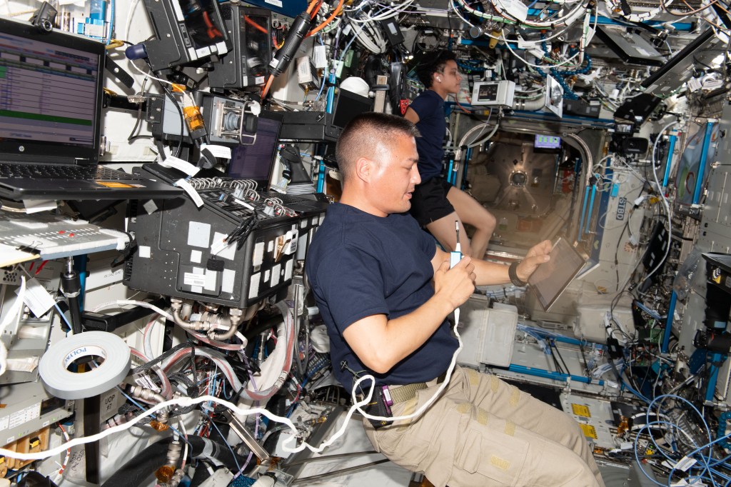 Expedition 67 Flight Engineers Kjell Lindgren and Jessica Watkins, both NASA astronauts, are pictured working on separate activities inside the International Space Station's U.S. Destiny laboratory. Lindgren reviews rendezvous and docking procedures on a touchscreen tablet the day before the arrival of Boeing's CST-100 Starliner crew ship. Watkins works out on an exercise cycle, also known as the Cycle Ergometer with Vibration Isolation and Stabilization, or CEVIS.