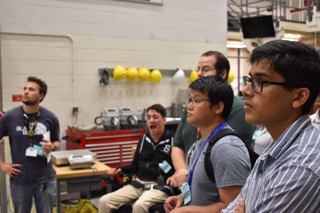 Medium perspective of a warehouse area. In the right foreground, a group of students pays close attention to their instructor [not pictured].