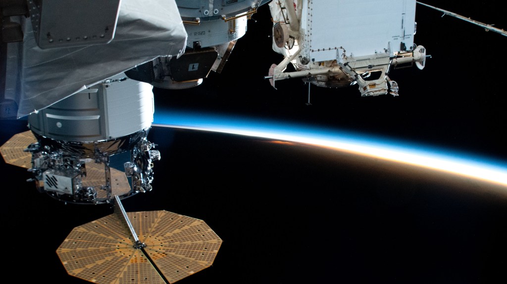 iss067e005680 (April 8, 2022) --- The Cygnus space freighter (left) from Northrop Grumman, with its prominent cymbal-shaped UltraFlex solar arrays, is pictured as the International Space Station flies into an orbital sunset 261 miles above the Pacific Ocean. At upper right, is a portion of the Rassvet mini-research module's docking port.