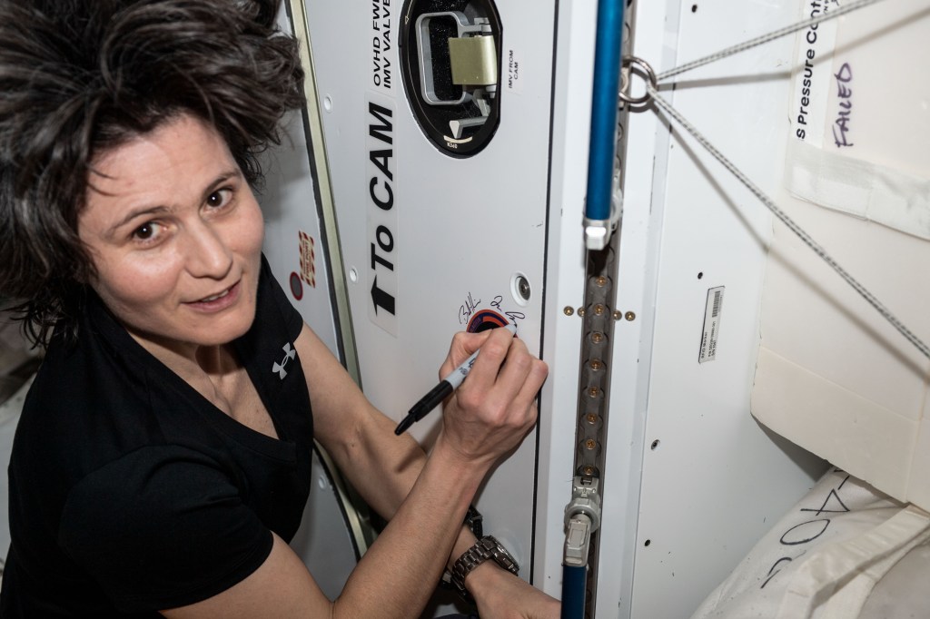 iss068e012464 (Oct. 5, 2022) --- ESA (European Space Agency) astronaut and Expedition 68 Commander Samantha Cristoforetti signs her name around the SpaceX CRS-25 mission insignia sticker affixed to the Harmony module's vestibule. Cristoforetti was aboard the International Space Station when the SpaceX Dragon resupply ship docked to Harmony's forward port on July 16, 2022, for a five-week cargo mission.