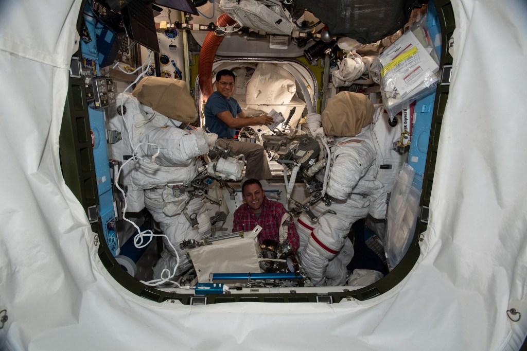 iss068e024215 (Nov. 23, 2022) --- NASA astronauts (from top) Frank Rubio and Josh Cassada configure spacewalking tools and components on a pair of Extravehicular Mobility Units (EMUs), or spacesuits, inside the International Space Station's Quest airlock.
