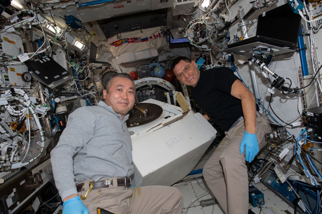 iss068e029529 (Dec. 13, 2022) --- Expedition 68 Flight Engineers (from left) Koichi Wakata of the Japan Aerospace Exploration Agency (JAXA) and Frank Rubio of NASA swap research hardware on the NanoRacks External Platform inside the Kibo laboratory module.