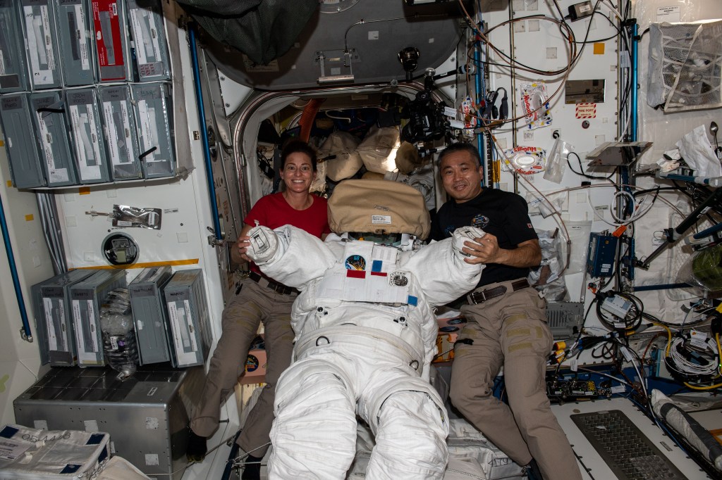 iss068e020601 (Nov. 3, 2022) --- Expedition 68 Flight Engineers Nicole Mann of NASA and Koichi Wakata of the Japan Aerospace Exploration Agency (JAXA) pose together with an Extravehicular Mobility Unit (EMU), also known as a spacesuit, inside the Unity module just outside the Quest airlock where spacewalks are staged with astronauts wearing the EMUs.