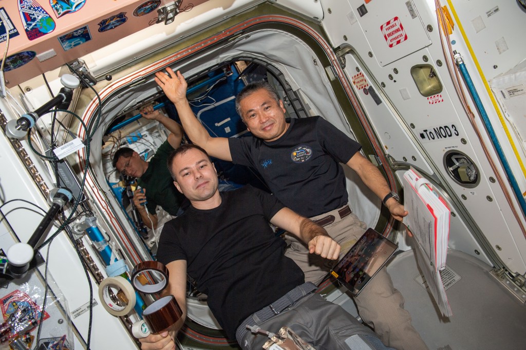 iss068e020531 (Nov. 3, 2022) --- Expedition 68 Flight Engineers (from left) Dmitri Petelin of Roscosmos and Koichi Wakata of the Japan Aerospace Exploration Agency (JAXA) pose for a portrait inside the International Space Station's Unity module. Behind the duo, is NASA astronaut and Expedition 68 Flight Engineer Frank Rubio at work inside the Tranquility module. Credit: Nicole Mann/NASA