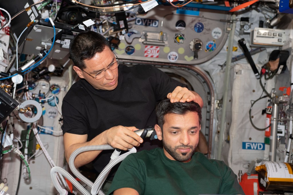 iss068e075695 (March 18, 2021) --- UAE (United Arab Emirates) astronaut Sultan Alneyadi receives a haircut from NASA astronaut Frank Rubio, both Expedition 68 flight engineers, aboard the International Space Station. The hair trimmer contains a suction device ensuring no loose hair contaminates the microgravity environment.