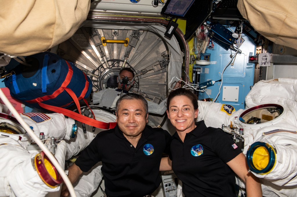 iss068e031327 (Dec. 21, 2022) --- Expedition 68 Flight Engineers Koichi Wakata of the Japan Aerospace Exploration Agency (JAXA) and Nicole Mann of NASA pose with a pair of Extravehicular Mobility Units (EMUs), or spacesuits, that NASA astronauts Frank Rubio and Josh Cassada (both out of frame) would wear during a spacewalk to install a roll-out solar array on the International Space Station's Port-4 truss segment.