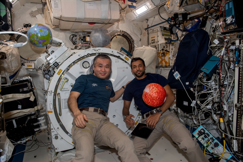 iss068e071153 (March 6, 2021) --- Expedition 68 Flight Engineers (from right) Koichi Wakata of JAXA (Japan Aerospace Exploration Agency) and Sultan Alneyadi of UAE (United Arab Emirates) pose with an inflatable ball in the image of Mars aboard the International Space Station's Kibo laboratory module.