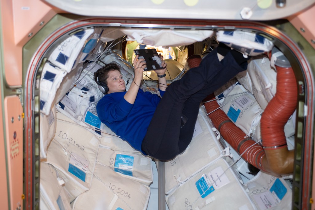 NASA astronaut Anne McClain relaxes with an electronic tablet on a Sunday morning inside the vestibule that connects the Unity module to the Zarya module.