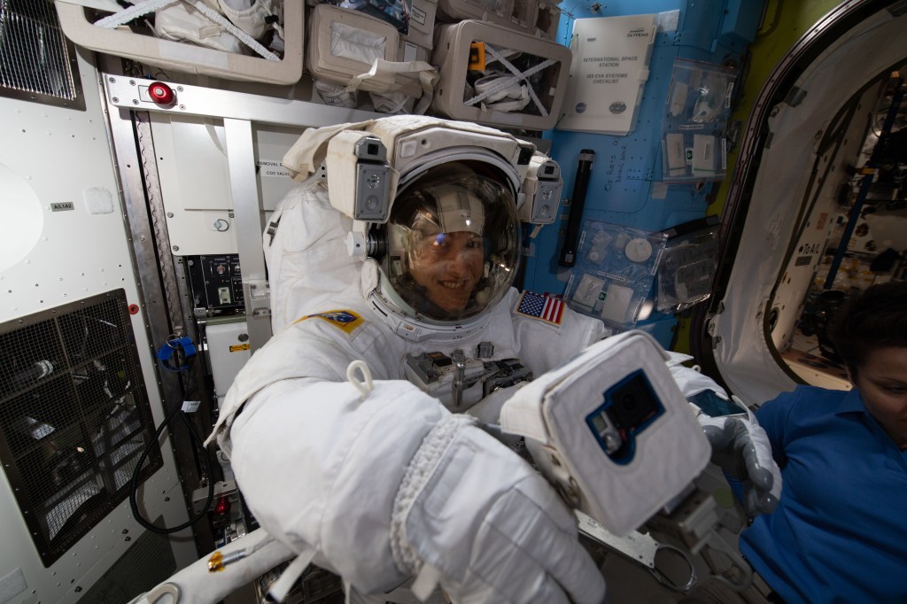 Inside the Quest airlock, NASA astronaut Christina Koch is fitted in a U.S. spacesuit and checks out a spacewalk camera less than two weeks before beginning her first spacewalk.