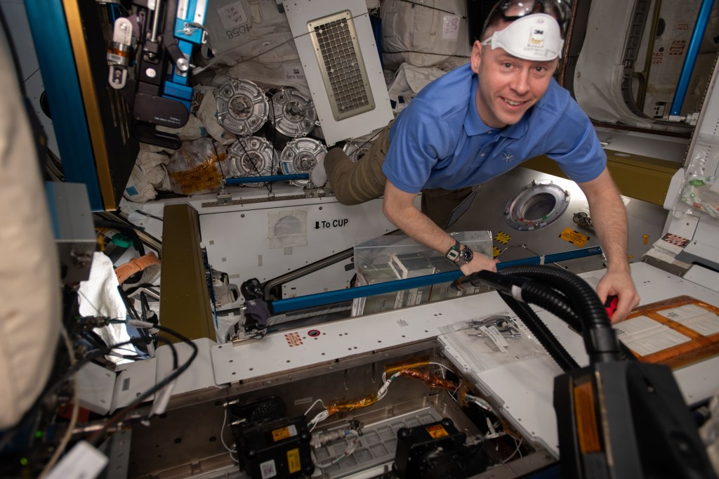 Expedition 59 Flight Engineer and NASA astronaut Nick Hague wears personal protection gear while working to remove bacteria filters and replacing them with charcoal filters inside the International Space Station's Tranquility module.