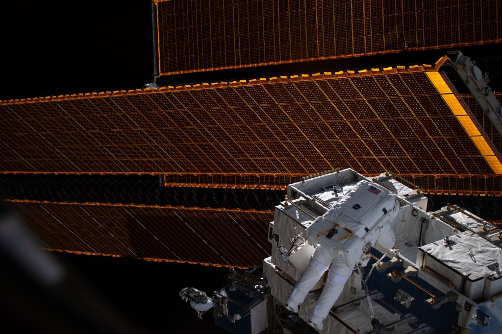 NASA astronaut Nick Hague, seemingly curtained by the International Space Station's solar arrays, retrieves batteries and adapter plates from an external pallet. He and NASA astronaut Anne McClain (out of frame) conducted a six-hour. 39-minute spacewalk to upgrade the orbital complex's power storage capacity on the Port-4 truss structure.