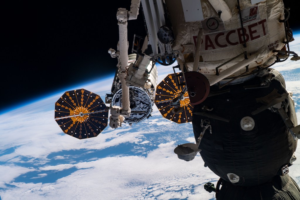 The Canadarm2 robotic arm controlled by NASA astronaut Anne McClain maneuvers to grapple the Northrop Grumman Cygnus cargo craft as the International Space Station orbited 256 miles above the Atlantic Ocean. Highlighting the foreground is the Soyuz MS-12 crew ship docked to the Rassvet module.