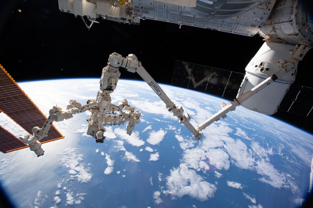 The Canadarm2 robotic arm with its robotic hand, also known as Dextre, attached for fine-tuned robotics work extends across the frame as the International Space Station orbited 256 miles above the Atlantic Ocean. The SpaceX Dragon resupply ship is pictured at right berthed to the Harmony module.