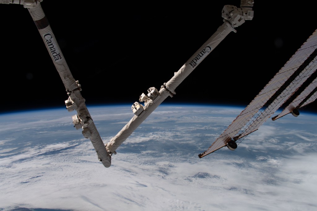 The Earth's limb and portions of the International Space Station's Canadarm2 robotic arm and solar arrays jut into the frame as the orbital complex flew 258 miles above the Great Lakes region of North America.
