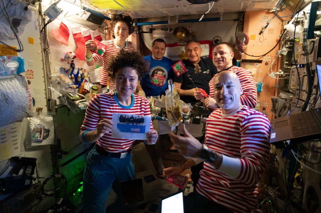 The Expedition 61 crew celebrates Christmas day with a brunch inside the International Space Station's Unity module decorated with stockings, flashlight "candles" and a Christmas tree banner. Clockwise from bottom left are, NASA Flight Engineers Jessica Meir and Christina Koch, Roscosmos Flight Engineers Oleg Skripochka and Alexander Skvortsov, NASA Flight Engineer Drew Morgan, and Commander Luca Parmitano of the European Space Agency (ESA).