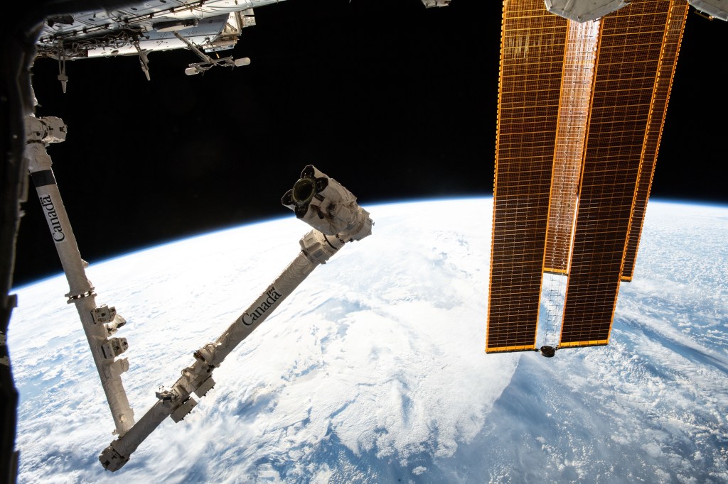The International Space Station's Canadarm2 robotic arm and solar array's highlight the foreground as the orbital complex flew 260 miles above the South Pacific Ocean northwest of New Zealand.