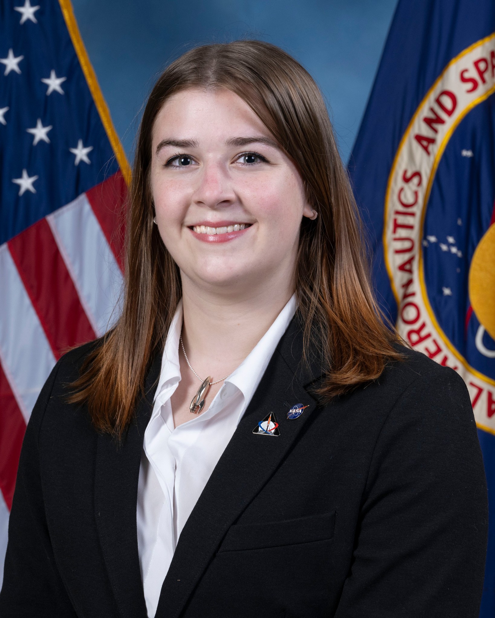 A woman with brown shoulder-length hair poses in front of the American and NASA flags for her headshot.