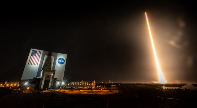 NASA's SpaceX Crew-8 can be seen lighting up the night sky after lifting off from Kennedy Space Center's Launch Complex 39A. To the left is the iconic Vehicle Assembly Building.