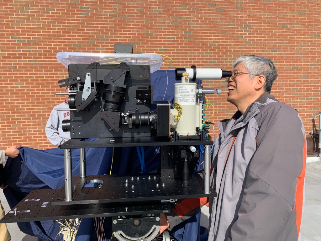 an engineer looks into an eyepiece connected to a large electronic instrument.