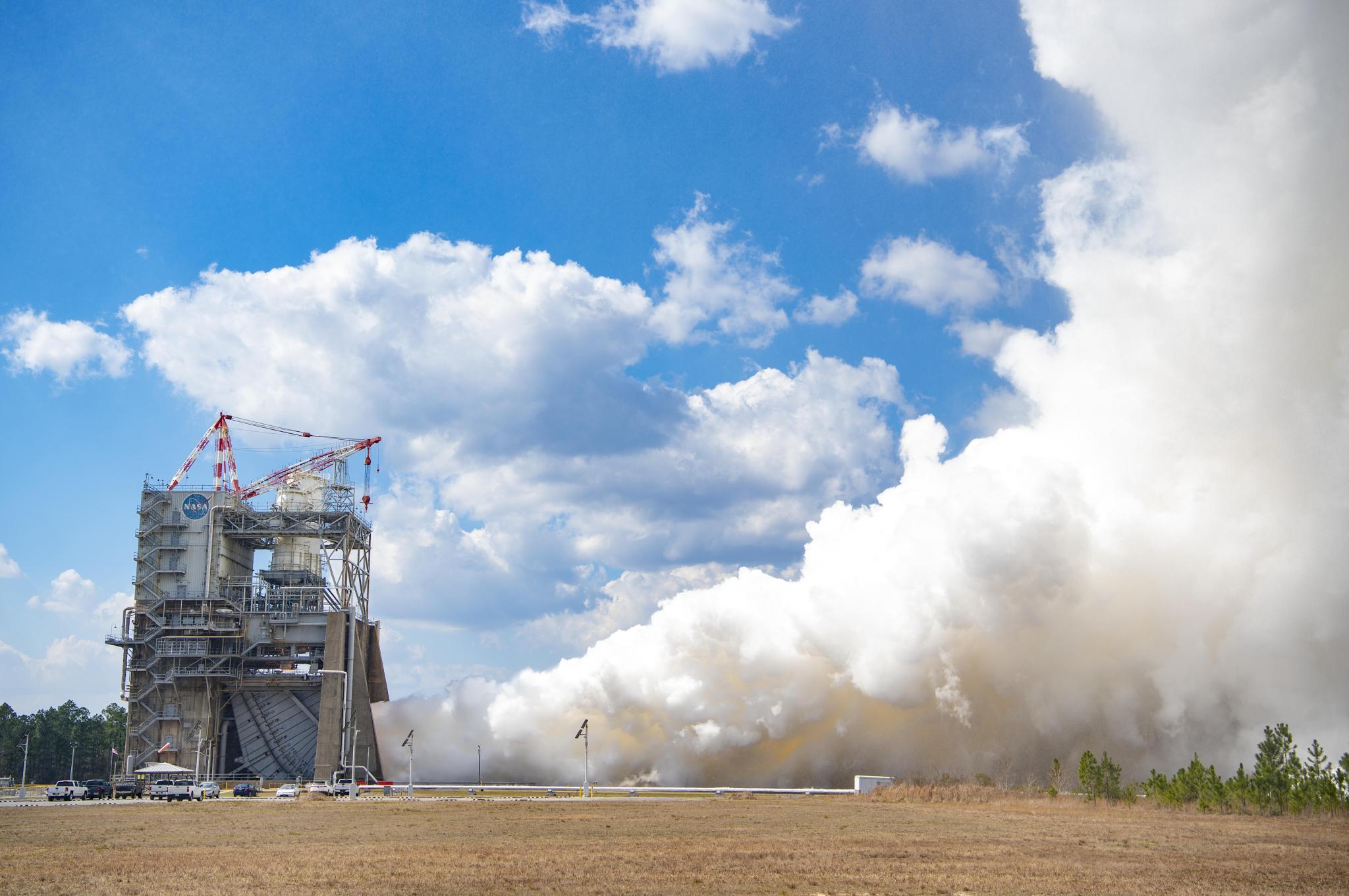vapor clouds erupt from a RS-25 hot fire; view is from across a grassy field