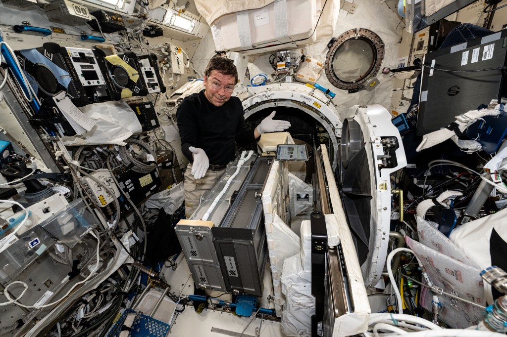 Expedition 71 Flight Engineer and NASA astronaut MIke Barratt poses for a portrait while installing a small satellite orbital deployer inside the Kibo laboratory module's airlock. The Japanese robotic arm will grapple the deployer and point it away from the station where it will release a series of CubeSats into Earth orbit for scientific and technology research.