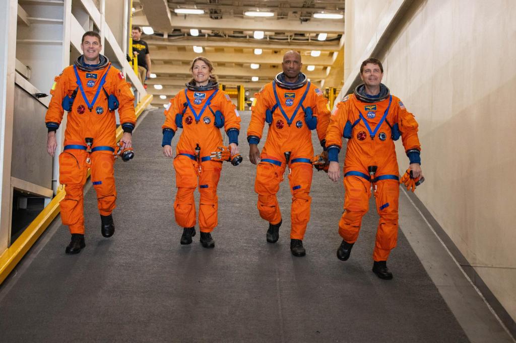 Four astronauts walk down a ramp in their orange suits.