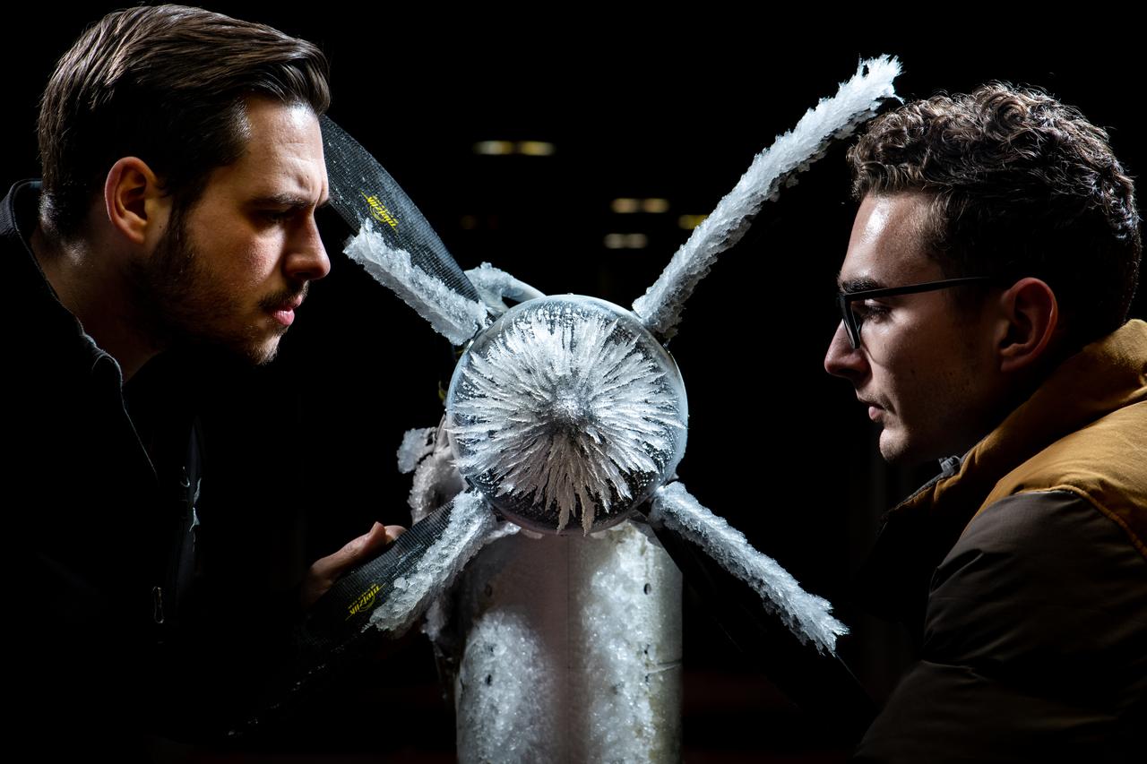 Two young men stare intently at ice formations on a spinner of a proprotor model.