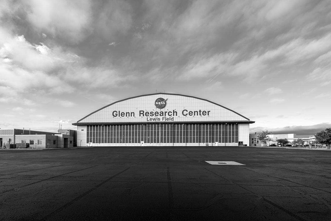 Black and white photo of the Glenn Research Center hangar that is in the distance. Clouds above the hangar look like they are moving fast.