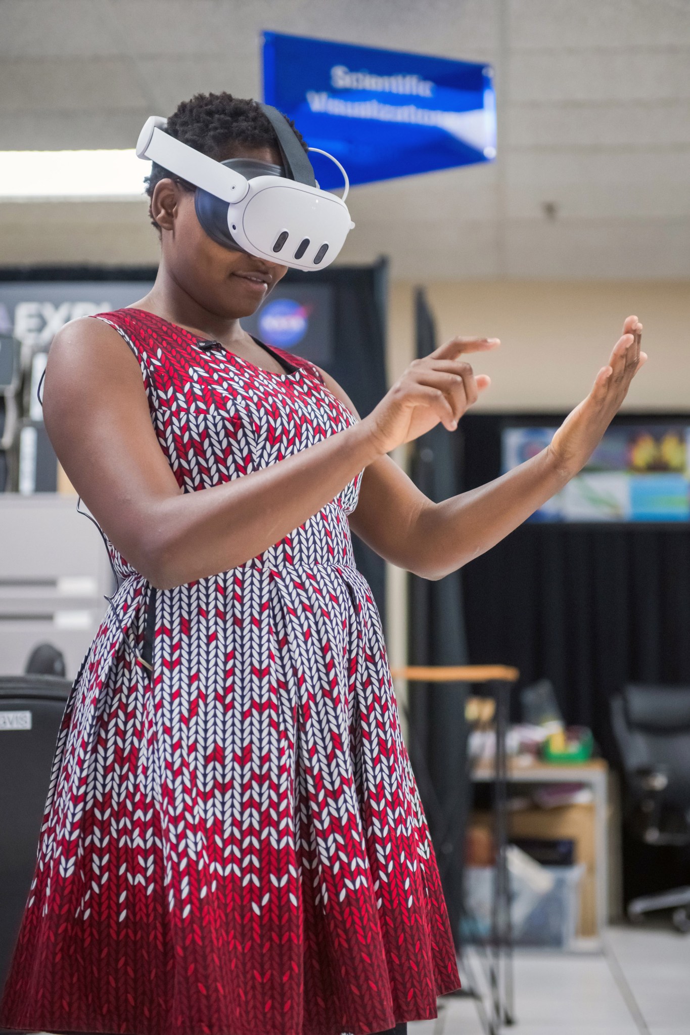 Nelly Cheboi在测试虚拟现实演示时集中精力。她戴着虚拟现实耳机，穿着红白相间的连衣裙。她的手看起来就像是在按下隐形平板电脑上的按钮。