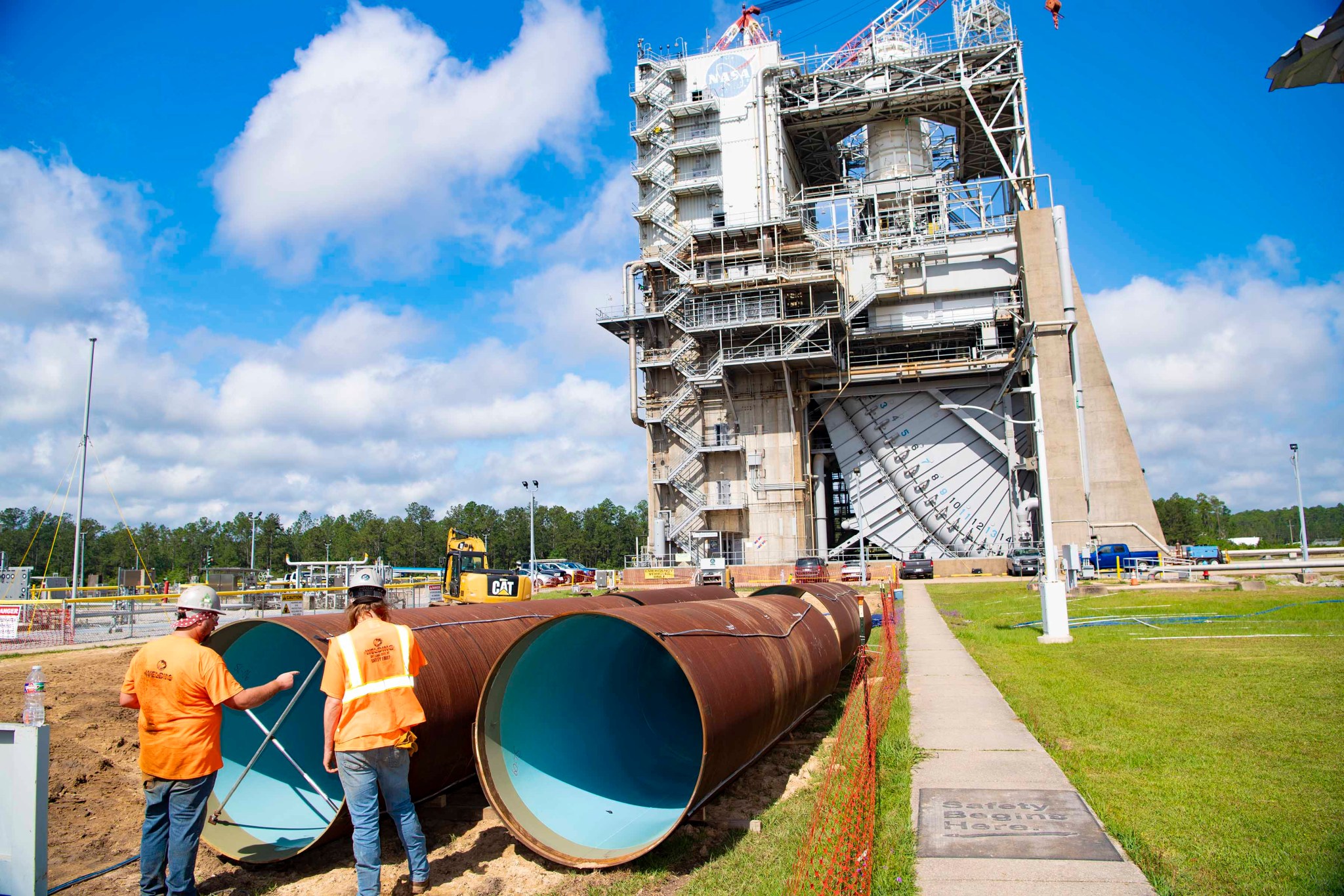 crew members are seen standing near new pipeline sections for upgrade; the Fred Haise Test Stand is seen in the background