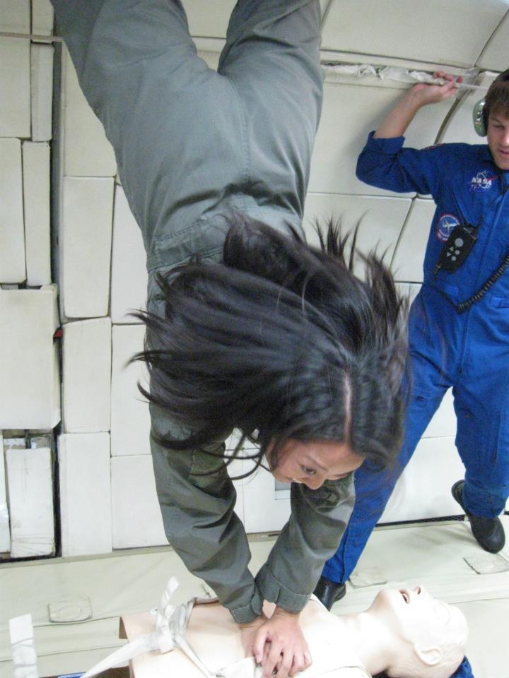 一名身穿浅棕色飞行服的女子在微重力中倒立着，双手抵住