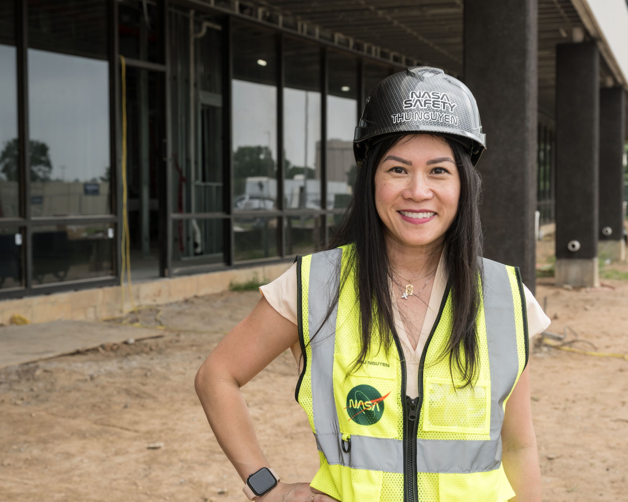 Fall Protection Program Administrator Thu Nguyen poses for a portrait wearing a yellow vest and hard hat outside Building 31x, a construction site at NASA's Johnson Space Center.