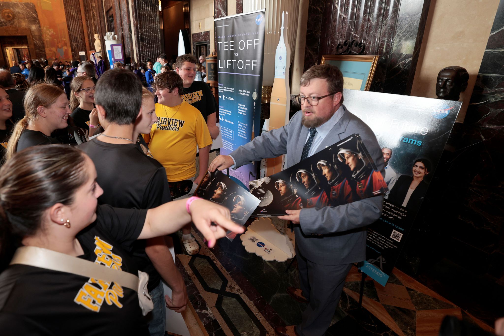 Lockheed Martin Multi-Functional Manufacturing Associate Manager Corey Riddle hands out Artemis II crew posters and talks Orion production with students and visitors at the Louisiana State Capitol.