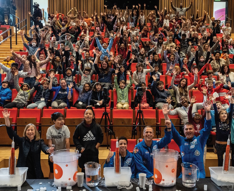 An auditorium filled with students, Astronauts and leadership raising their hands