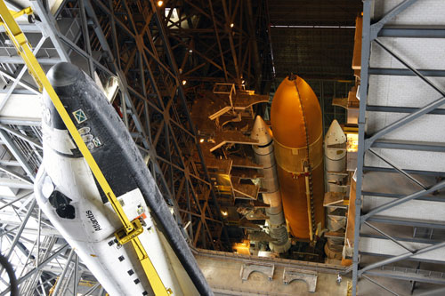 In the Vehicle Assembly Building (VAB) at NASA's Kennedy Space Center in Florida, workers lift Atlantis to mate it to its External Tank and Solid Rocket Boosters