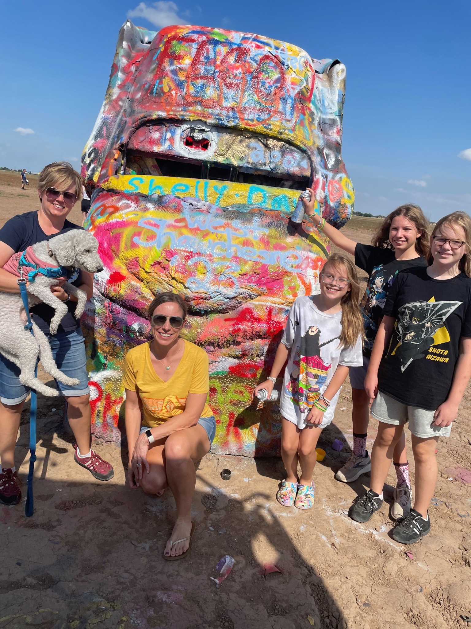 A family of five - two moms and three daughters - pose with their dog in front of a graffitied statue.