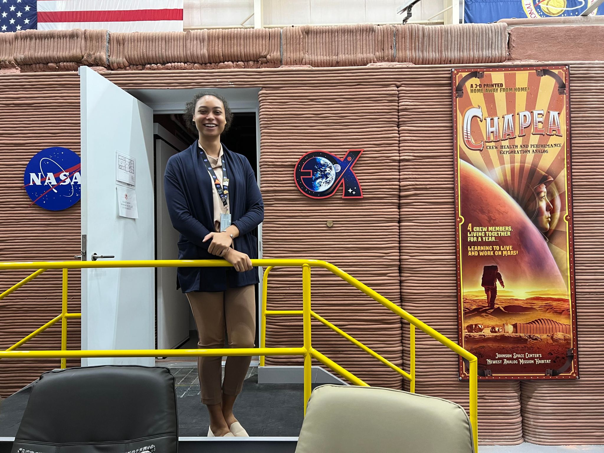 A young woman stands in front of the open door of a simulated Mars habitat at Johnson Space Center.