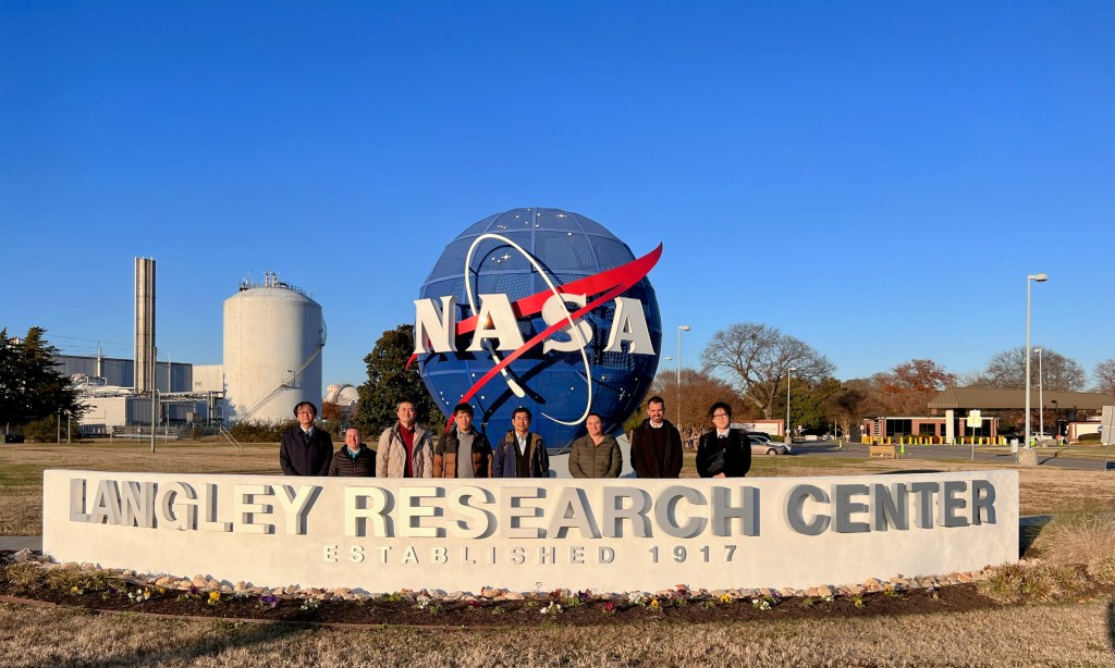 Eight researchers stand outside in front of NASA meatball statue and behind a sign that reads “Langley Research Center established 1917."