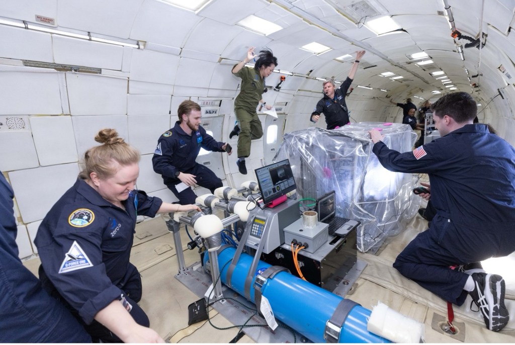 五个穿着飞行服的人在模拟月球重力环境中漂浮，进行实验。