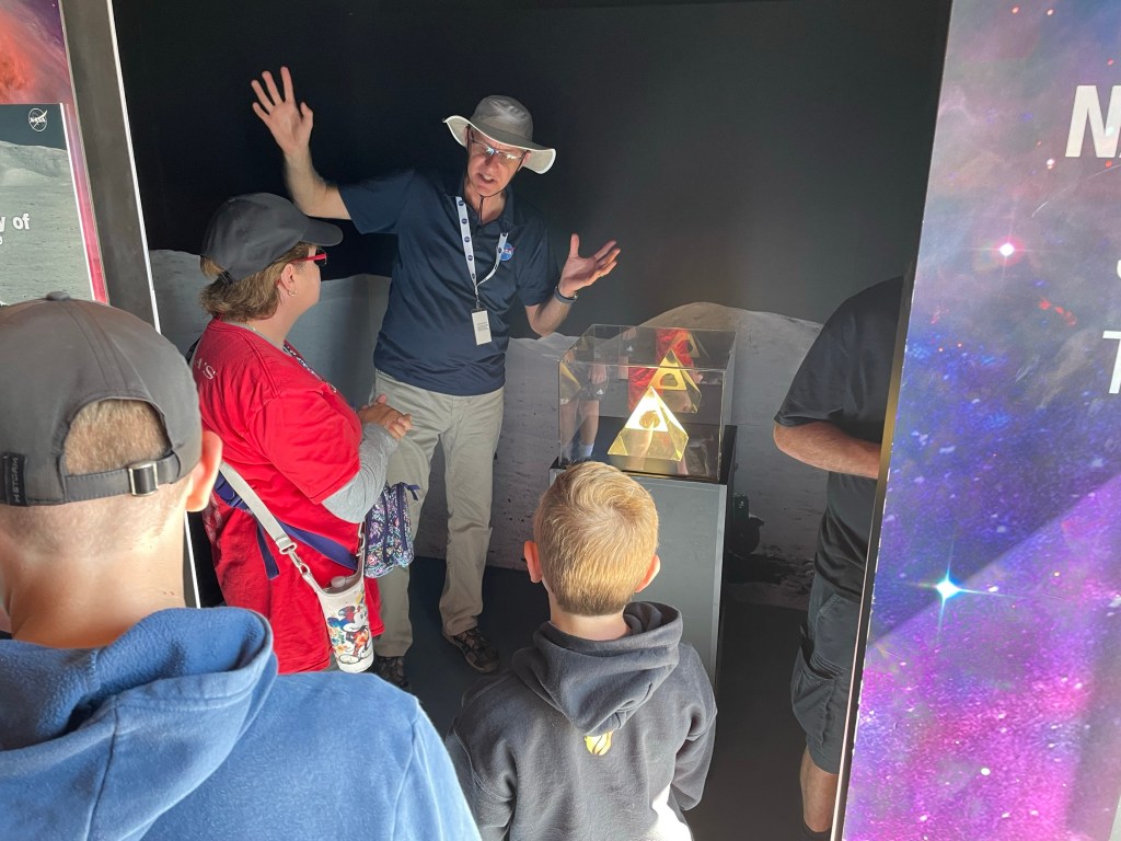 An animated NASA solar system specialist explains features of a moon rock to visitors gathered in front of him in the Journey to Tomorrow traveling exhibit.