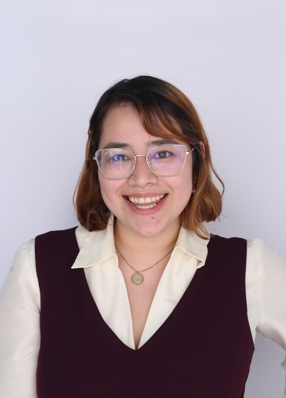 Professional portrait of a young woman wearing silver-rimmed glasses, a cream collared blouse, and an eggplant-colored vest.
