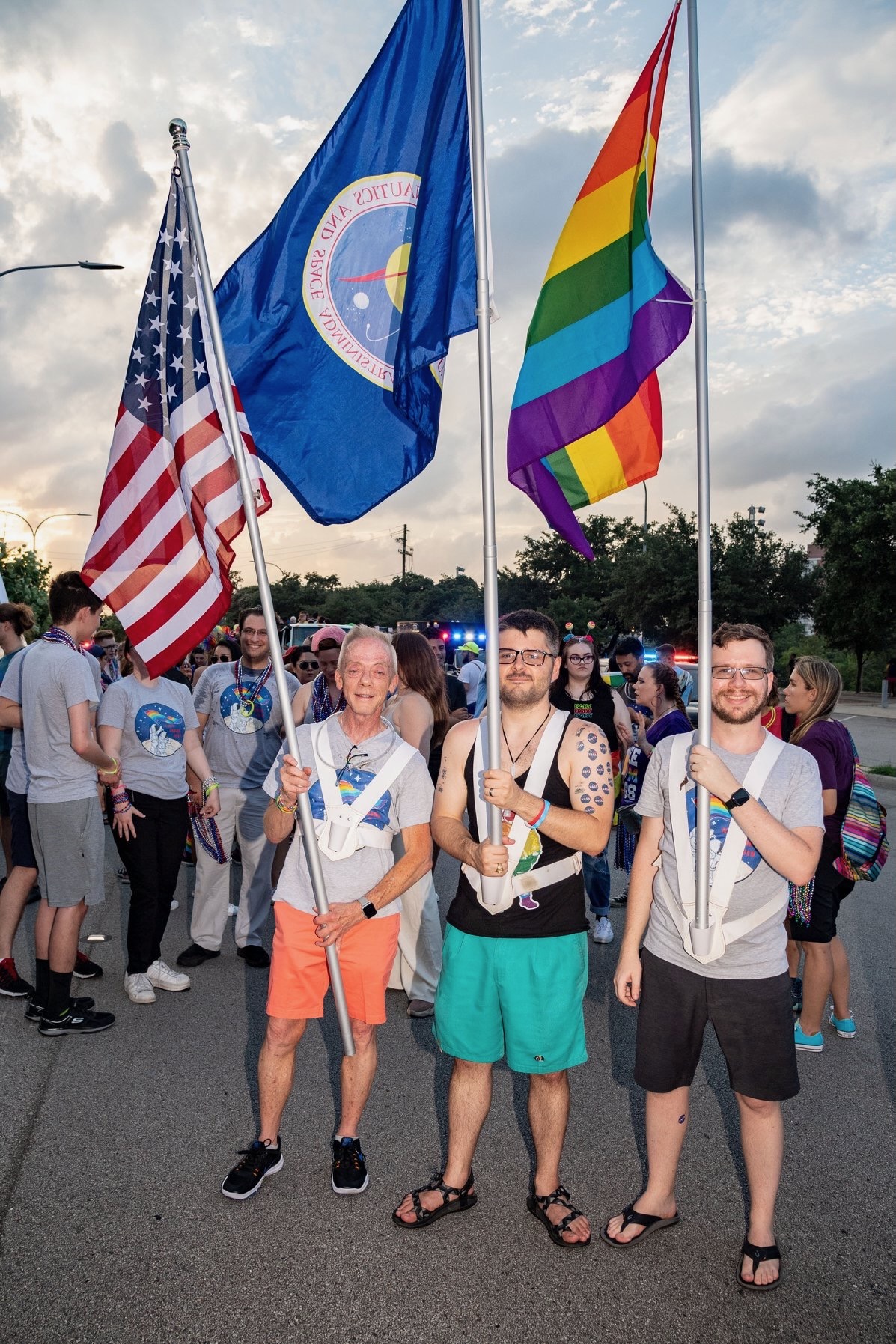 Three men hold a U.S., NASA, and Pride flag as they prepare to march in Houston's annual Pride Parade.