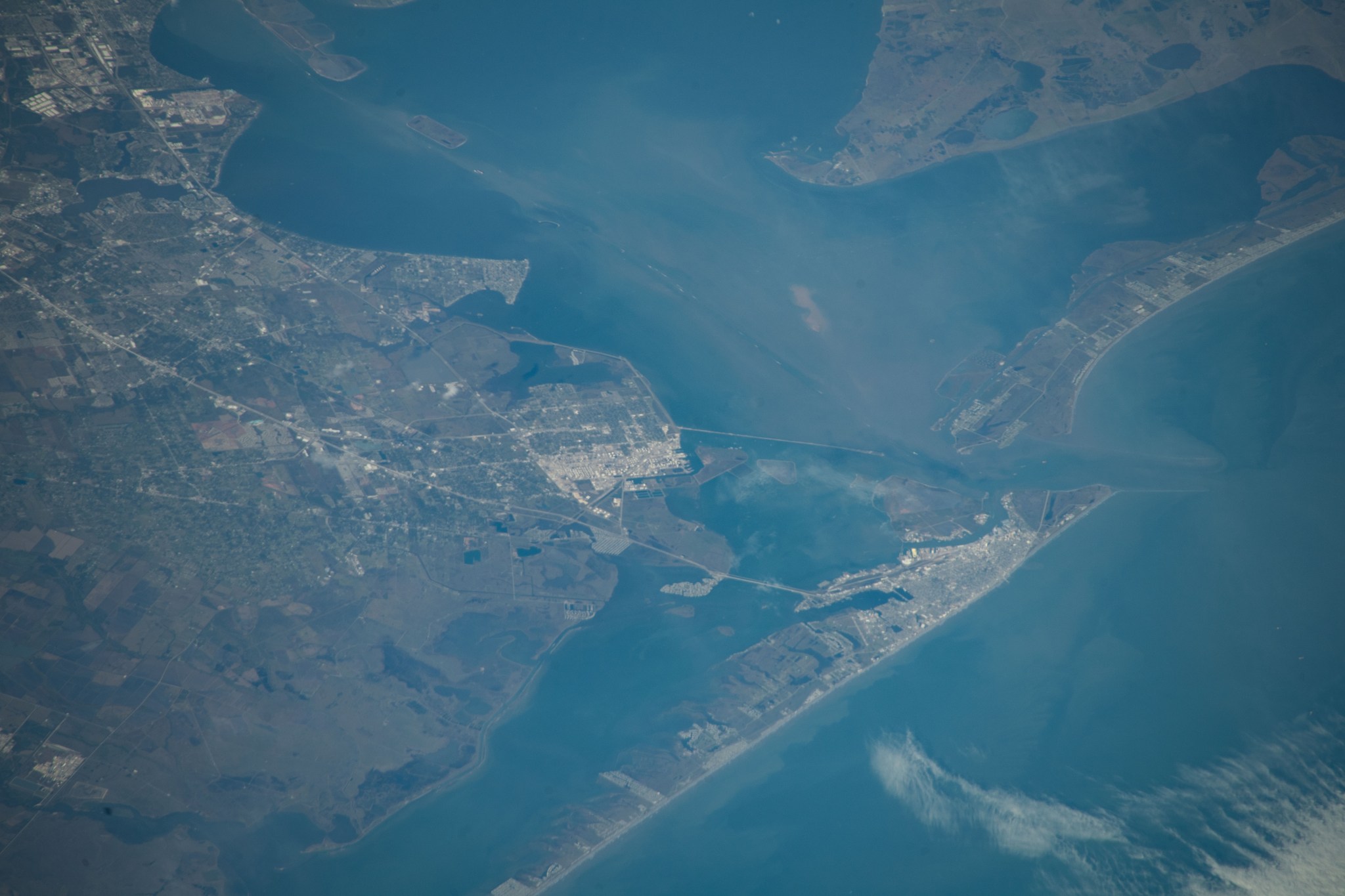 A view of Galveston from the International Space Station. The colors are faded: the land is a muted green, while the water is a hazy blue.